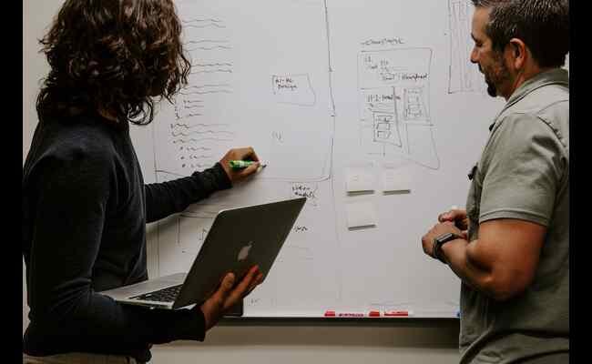 Two people at a whiteboard, one with a laptop and one without, discussing the results from a parallel coordinate plot.